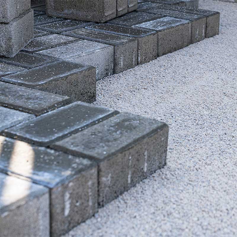Gray rectangular brick pavers being arranged on gravel.