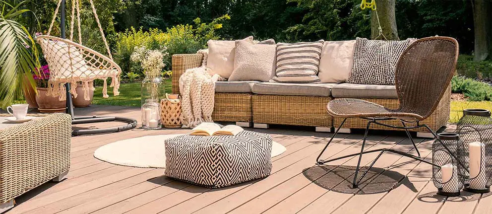 A deck furnished with an outdoor couch with pillows, other single chairs and oversized candles.