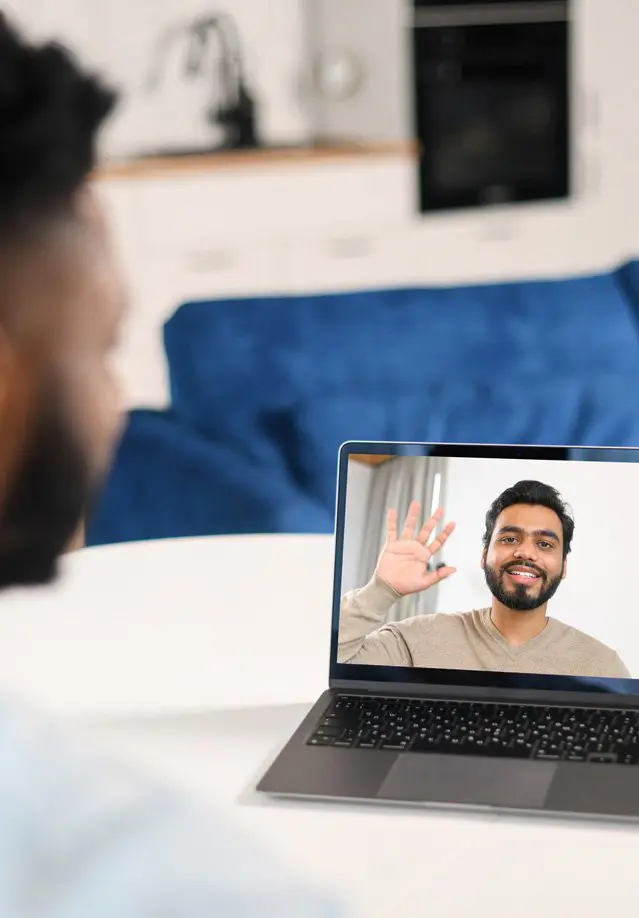 Waist up view of the young man in blue shirt waving with hand and saying hello while chatting via laptop with male colleague from home